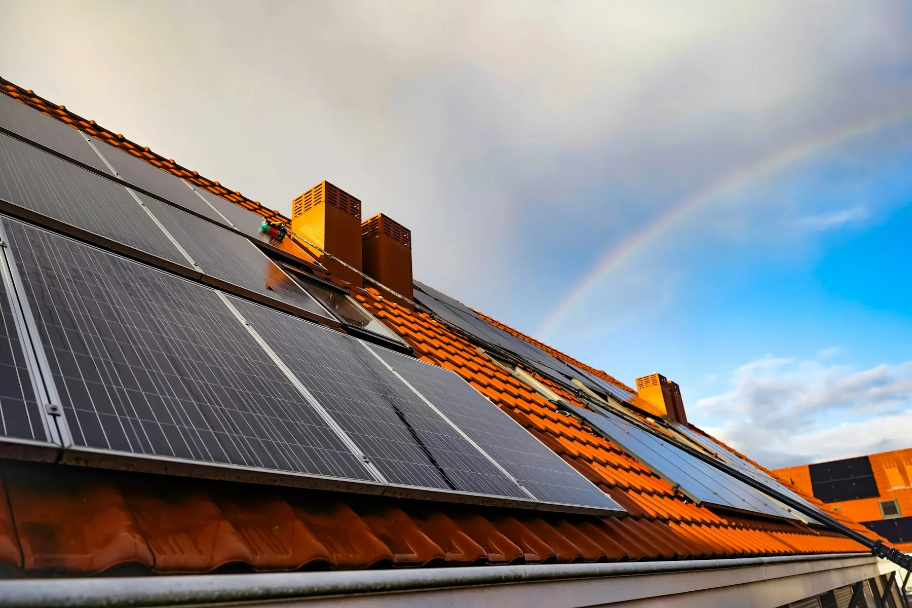 Toit en tuiles équipé de panneaux solaires sous un arc-en-ciel